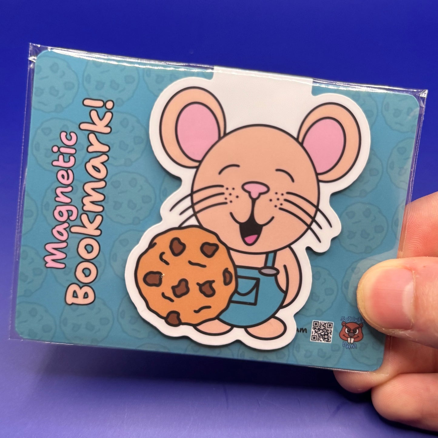 Magnetic bookmark with cartoon mouse holding a cookie, held by a hand against a blue background
