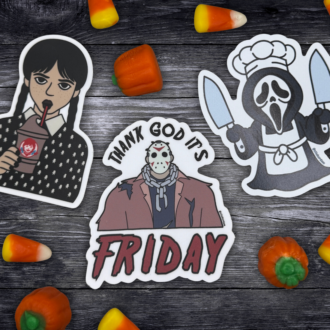 Wednesday Addams sticker, Jason Vorhees sticker, and Ghostface magnet on a gray table surrounded by candy corn