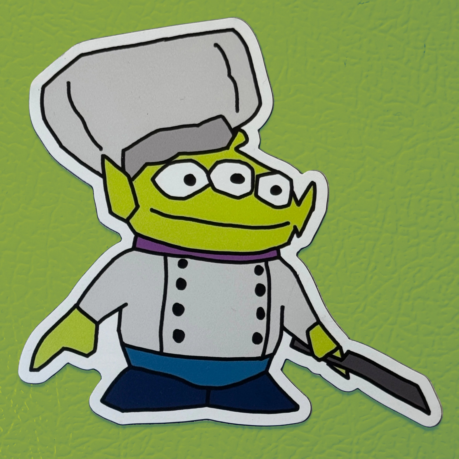 Alien Chef vinyl fridge magnet parody design – green three-eyed alien wearing chef hat holding knife on green background.