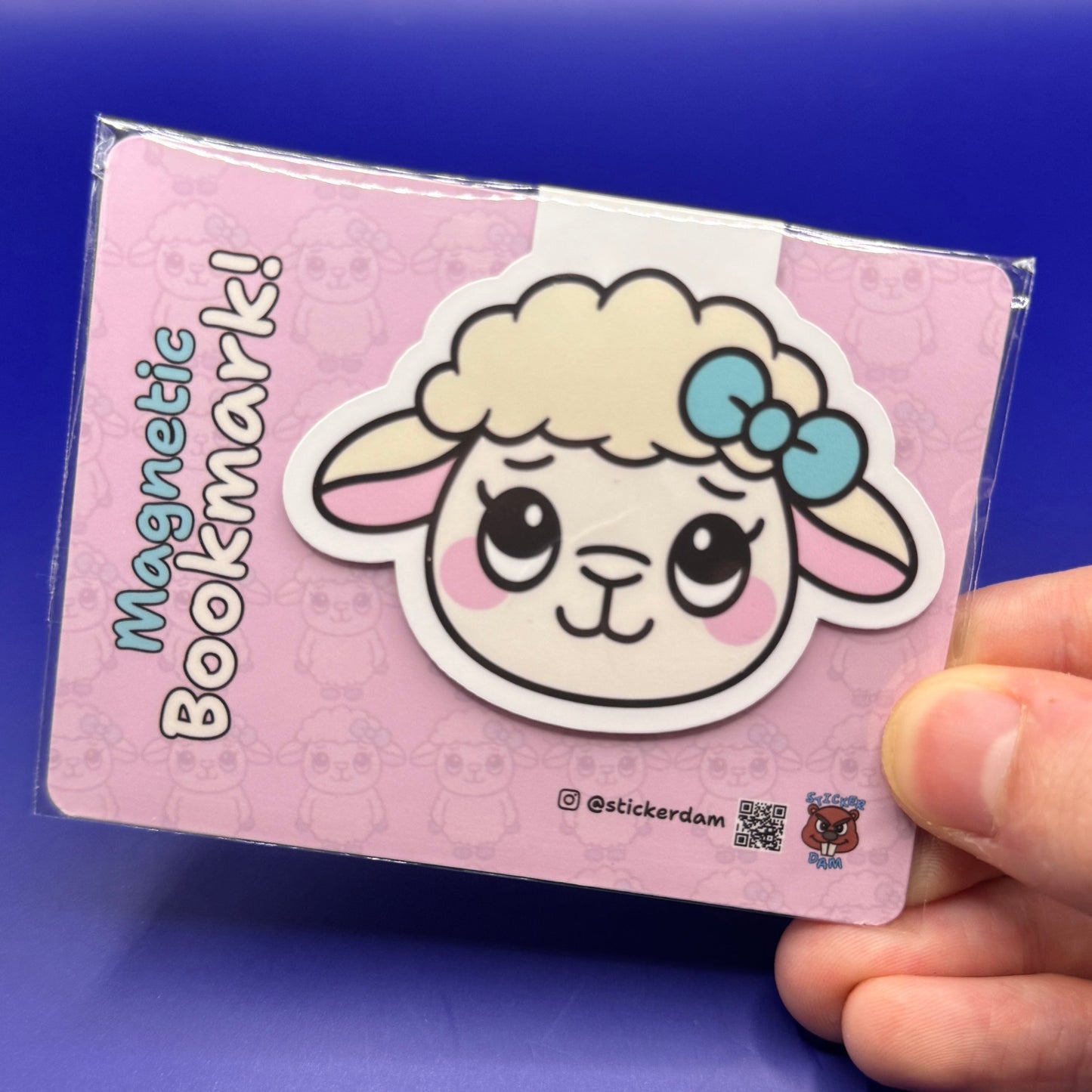 Magnetic bookmark with a cartoon sheep design held by a hand against a blue background