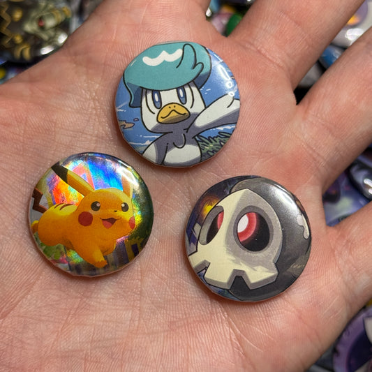 Three upcycled Pokémon card buttons featuring Quaxly, Pikachu, and Duskull resting in an open palm.